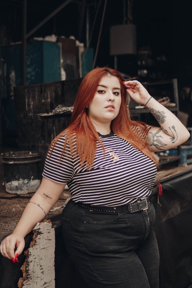 femme ronde aux cheveux longs roux dans une tenue sobre mais avec des détails esthétiques voyants