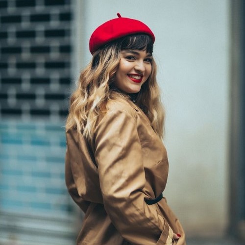 femme souriante avec 2 couleurs de cheveux différentes et un beret rouge assorti à son rouge à lèvres
